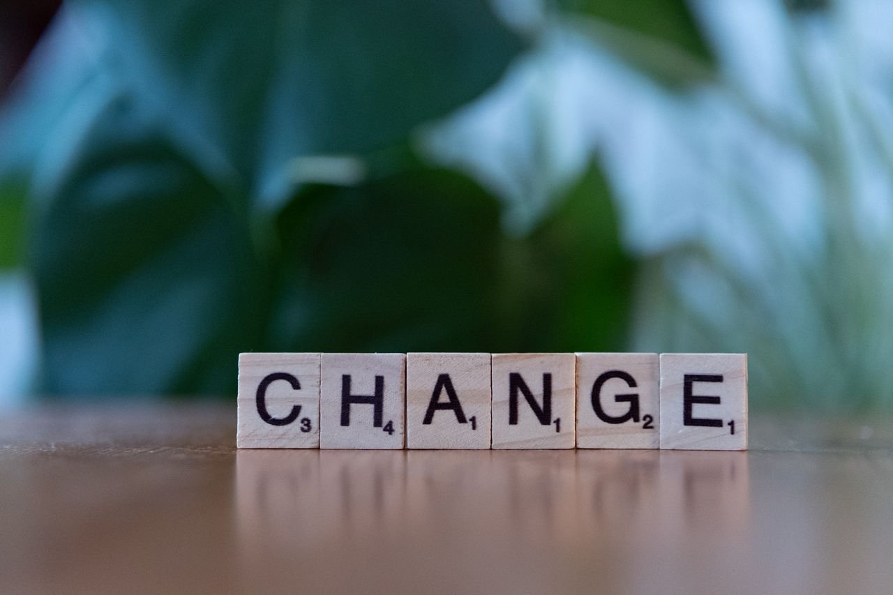 Scrabble tiles spelling 'CHANGE' on a wooden surface with a blurred green background.
