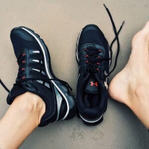 A pair of black sneakers next to bare feet on a gray surface.